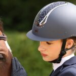 A rider wearing a riding hat standing by a horse