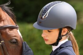 A rider wearing a riding hat standing by a horse