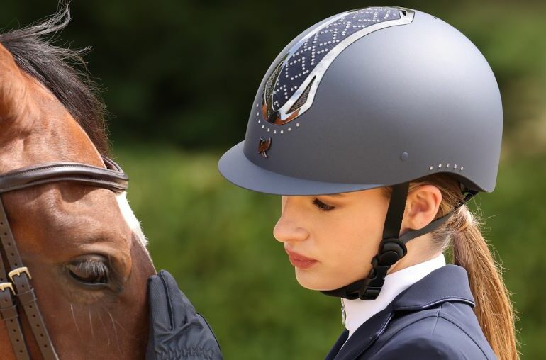 A rider wearing a riding hat standing by a horse