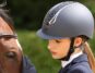 A rider wearing a riding hat standing by a horse