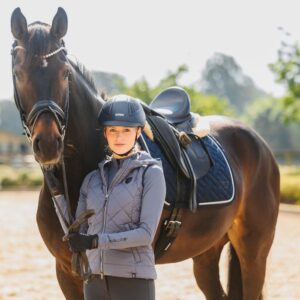 A rider wearing a Uvex riding hat standing by a horse
